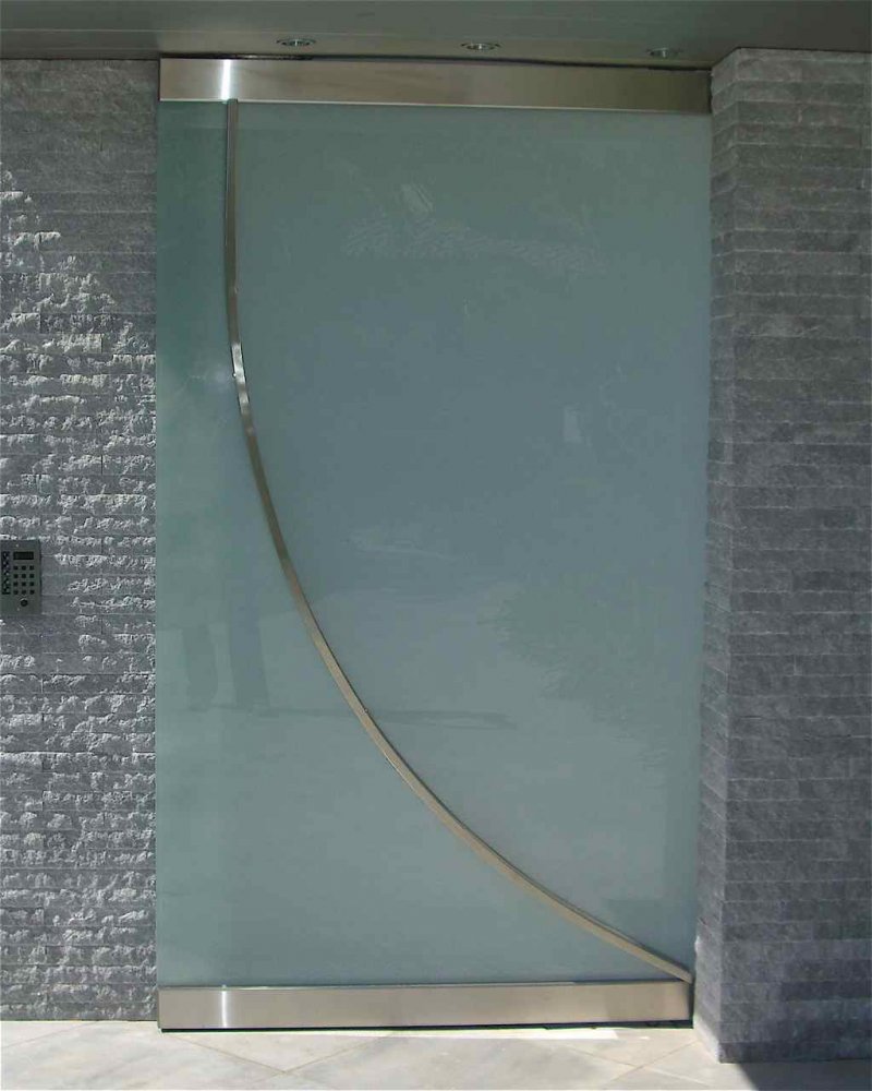 This stunning glass entry gate is made up of white laminated glass, with stainlless steel header and footer witha swooping steel handle, running diaginally curved across the entire height.