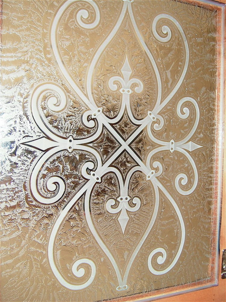 A close up view of the carved wrought iron motif, kitchen cabinet glass with a gluechipped background.